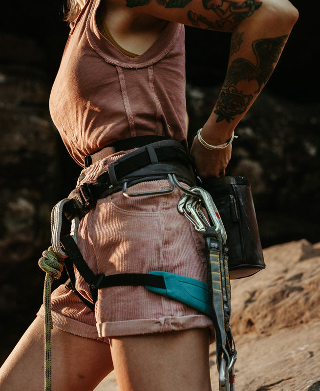 a woman is pictured with a climbing harness and gear on while putting her hands in the so ill x on the roam black chalk bag