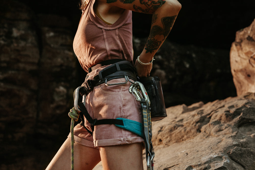 a woman is pictured with a climbing harness and gear on while putting her hands in the so ill x on the roam black chalk bag